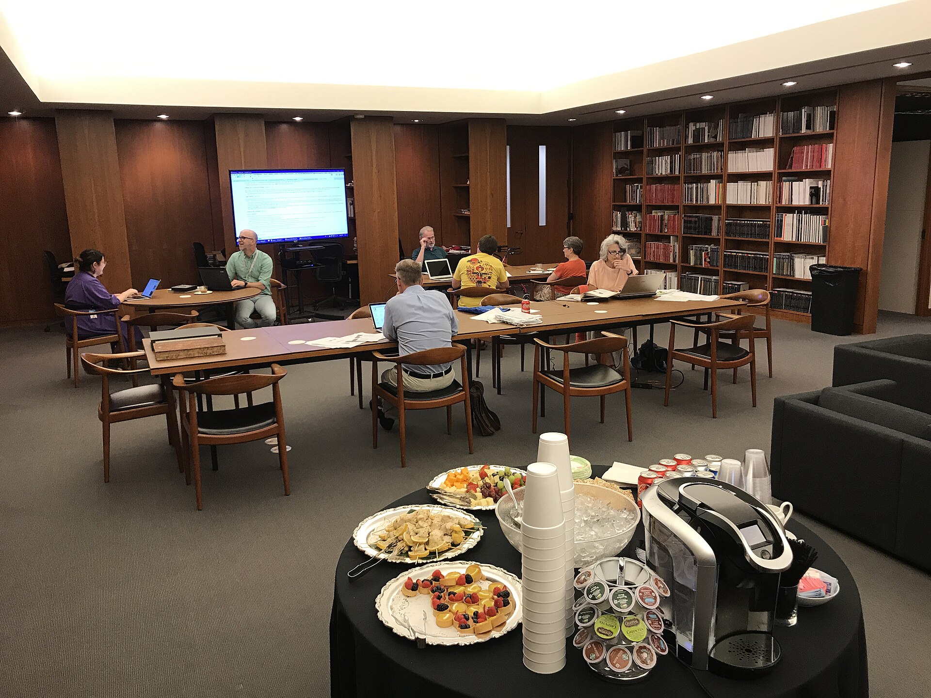 People working and talking around long tables in a library room